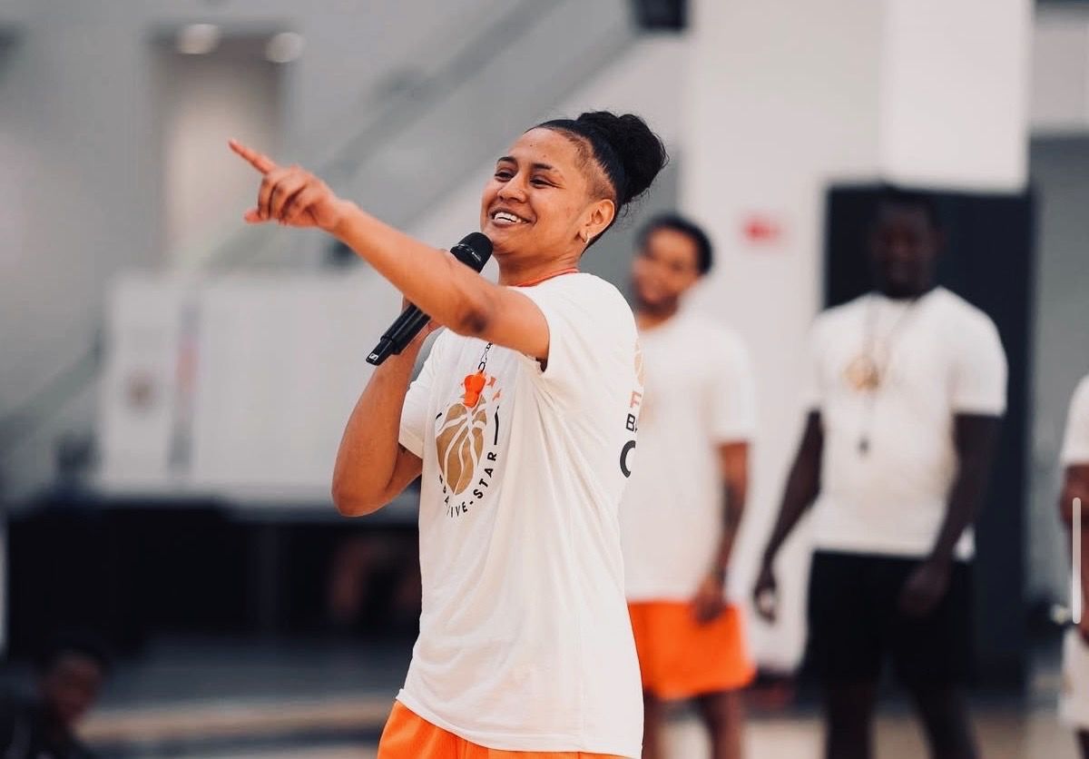 Coach Nay with a microphone, pointing to a player across the gym